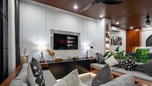 Ein modernes Wohnzimmer mit einem großen Flachbildfernseher an der Wand, einer Holzbalkendecke und einer festen Bank entlang der Wand.