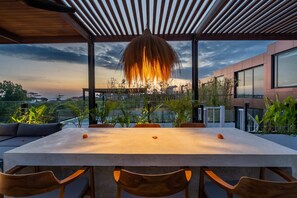 A modern outdoor dining area with a large table and chairs, surrounded by plants and a view of the cityscape. - Villa Sevu 6 (Cemagi)