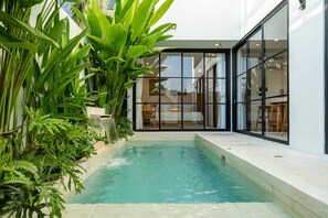 An indoor swimming pool with a glass wall, surrounded by lush green plants. - Villa Sevu 2 (Cemagi)