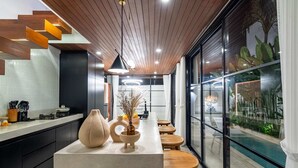 A modern kitchen with a long island, wooden stools, and a view of an indoor pool. - Villa Sevu 4 (Cemagi)