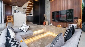 A modern living room with a grey sofa, a TV, and a kitchen area in the background. - Villa Sevu 4 (Cemagi)