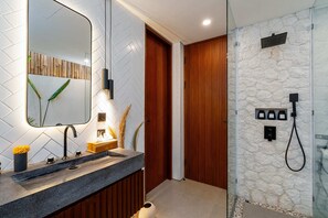 Ein modernes Badezimmer mit einem Granitwaschbecken, einem Holzschrank zur Aufbewahrung, einem großen Spiegel und einer Duschkabine aus Naturstein.