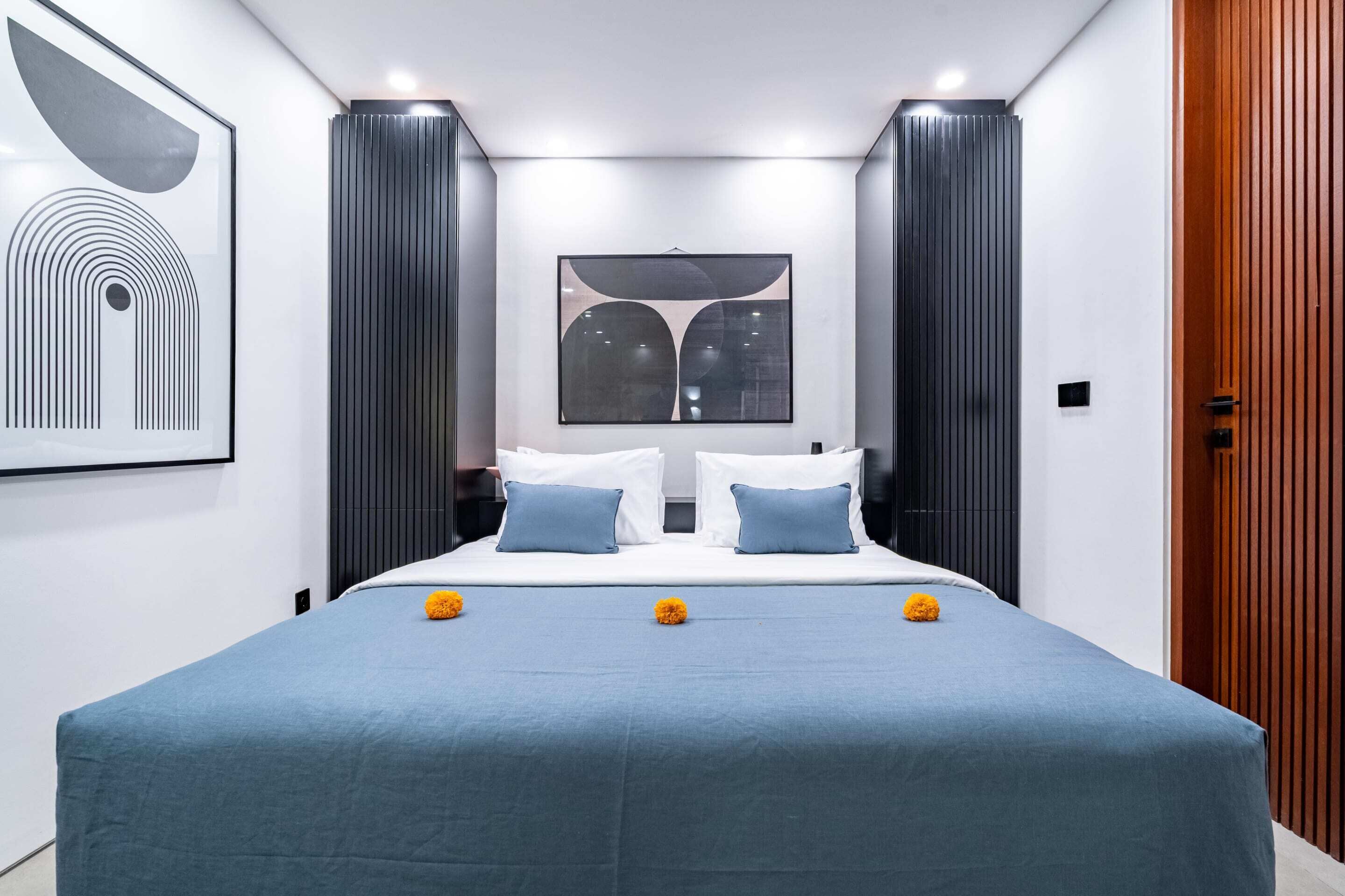 A modern bedroom with a large bed, two pillows, a blue bedspread, and decorative flowers.