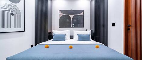 A modern bedroom with a large bed, two pillows, a blue bedspread, and decorative flowers.
