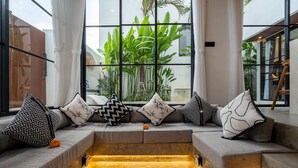 A modern living room with a built-in heated floor, large windows with a view of tropical plants, and a wooden ladder. - Villa Sevu 4 (Cemagi)