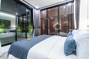 Ein modernes Hotelzimmer mit einem großen Bett, Blick auf Grün hinter raumhohen Fenstern und einer stilvollen Einrichtung.