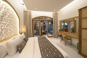 A modern bedroom with a large bed, a desk, and a view of a balcony. - Villa Jackie O (Seminyak)