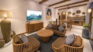 A modern living room with a round wooden coffee table, wicker sofas, and a TV mounted on the wall. - Villa Jackie O (Seminyak)