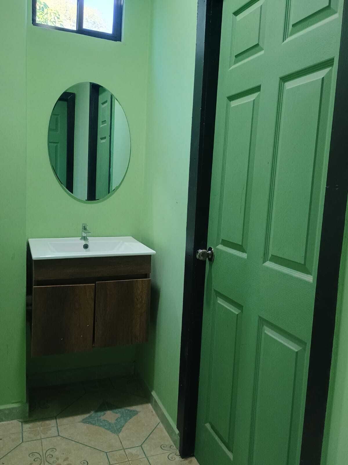 Une salle de bain avec une porte verte, un miroir rond et un meuble-lavabo en bois avec un évier blanc.