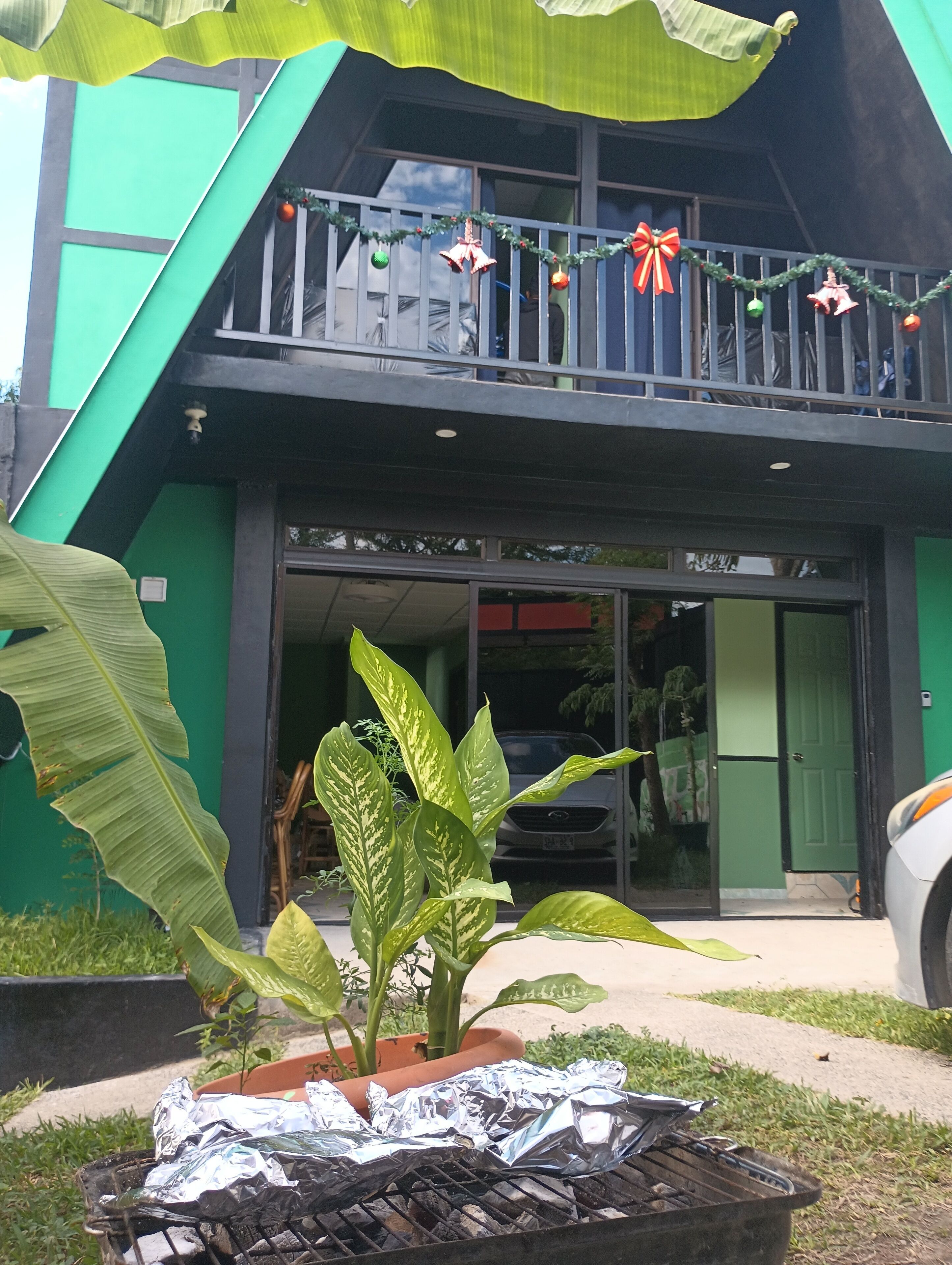 Um edifício com fachada verde, uma varanda decorada para o Natal e uma churrasqueira na parte externa.