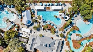Una vista aerea di un resort con diverse piscine, aree relax e un edificio imponente con un tetto caratteristico.