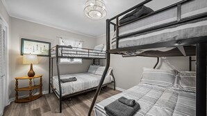 Et sovesalværelse med køjesenge, et træsidebord med en lampe og et billede i ramme på væggen.
