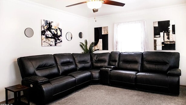 A modern living room with a black leather sectional sofa, a ceiling fan, and abstract wall art.