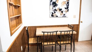 A dining area with a wooden table and four chairs, a wooden bench, and a wall-mounted abstract painting.