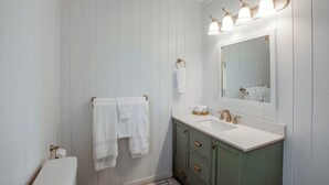 A bathroom with white walls, a white sink, and a green vanity. There are three light fixtures above the mirror and a towel rack with two towels.