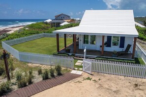 Une maison située sur la côte, avec une façade blanche, un patio couvert et une vue sur l’océan.
