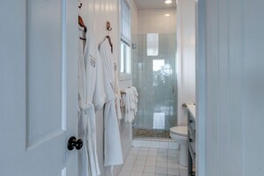 Une salle de bain avec des murs recouverts de carreaux blancs, une douche en verre et des toilettes.