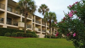 Een meerlaags hotel met balkons, palmbomen en verzorgde gazons.