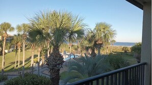 Een balkon met uitzicht op een zwembad, palmbomen en een strand in de verte.