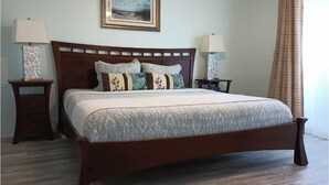 Een netjes opgemaakt bed met een houten hoofdbord, twee nachtkastjes met lampen en een lijst met een afbeelding aan de muur.