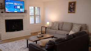 A living room with a fireplace, a sofa, a coffee table, and a television mounted on the wall. - Comfortable Home Near CoxHealth & MSU - Fenced Yard (Springfield)