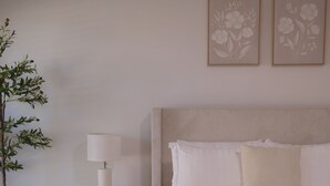 A bedroom with a wooden nightstand, a lamp, a bedside table, a bed with white bedding, and a potted plant. - Comfortable Home Near CoxHealth & MSU - Fenced Yard (Springfield)