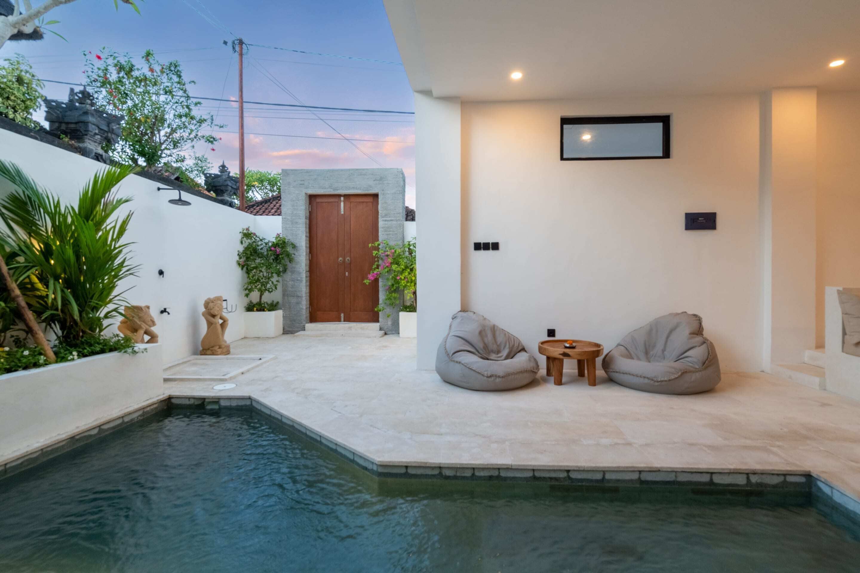 A modern outdoor pool area with two bean bags, a small table, and a wooden door.