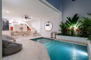 Un área de piscina interior moderna con una escalera, un sofá y un sillón informal.