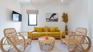 A modern living room with a sofa, two wicker chairs, a round table, and a large woven light fixture. - Villa Ombak (Cemagi)