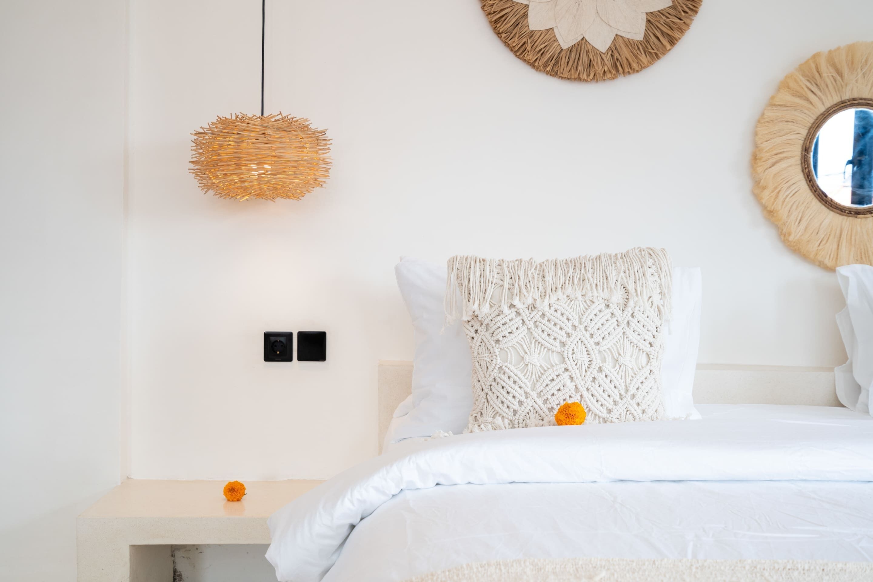A bedroom with a bed, a bedside table, a wall-mounted light, and a round mirror.