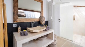 A bathroom with a wooden-framed mirror, a stone sink, and a towel rack. - Villa Imbuh 1 (Canggu)