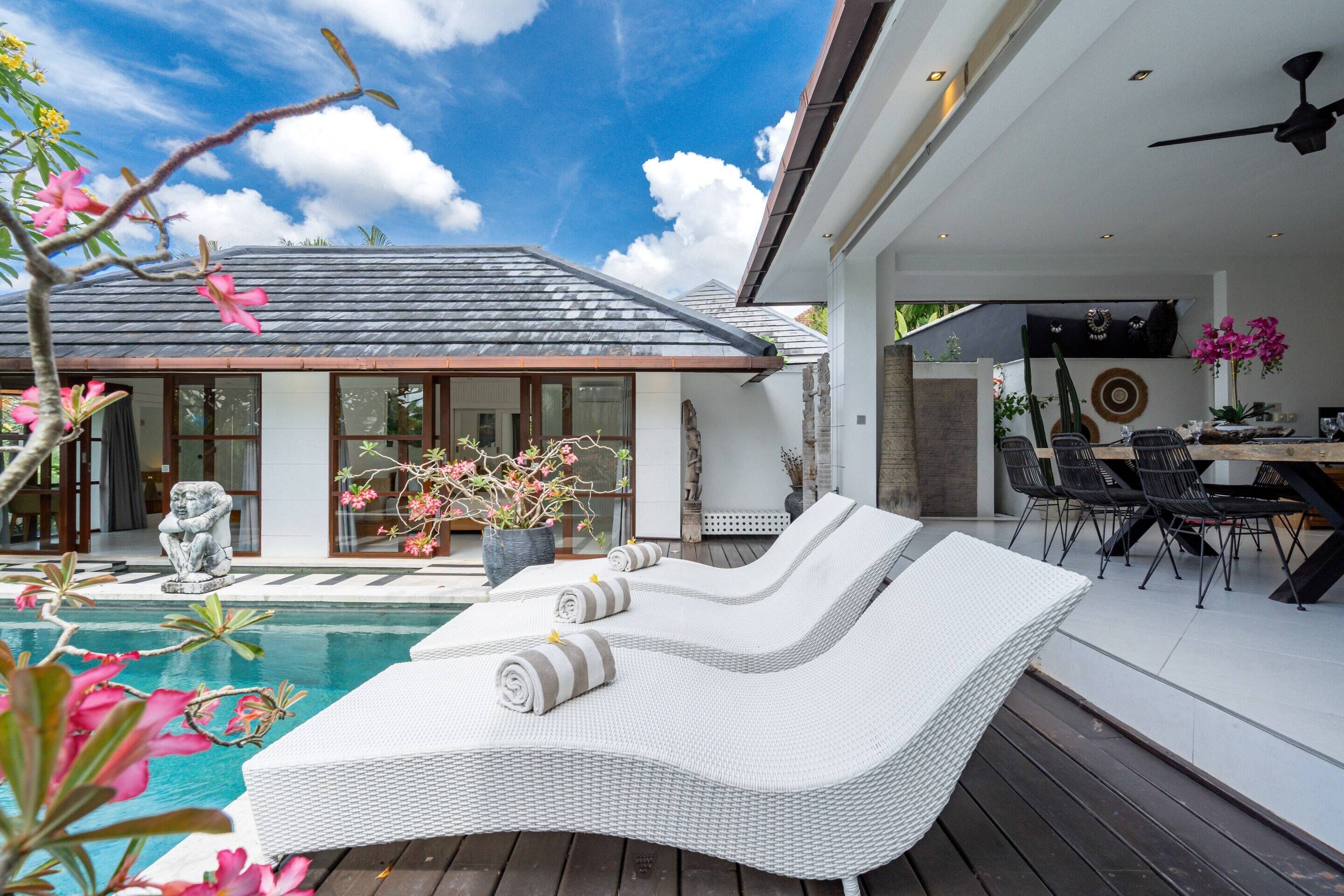 A modern outdoor pool area with lounge chairs, a dining table, and a statue.