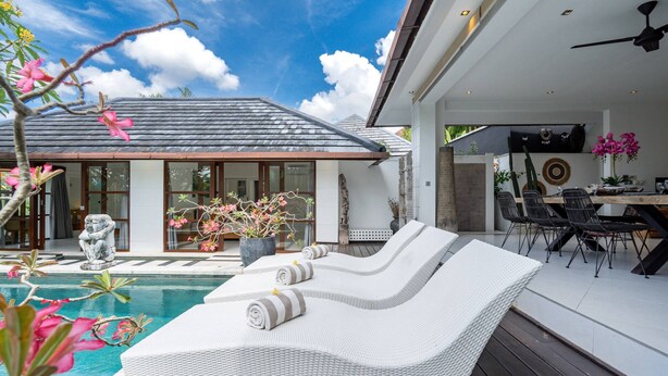 A modern outdoor pool area with lounge chairs, a dining table, and a statue. - Villa Imbuh 1 (Canggu)