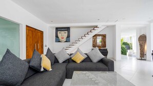 A modern living room with a grey sofa, a glass coffee table, and a staircase leading to another level. - Villa Imbuh 1 (Canggu)