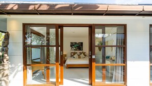 A hotel room with a bed, a painting, and a view of the outside. - Villa Imbuh 1 (Canggu)