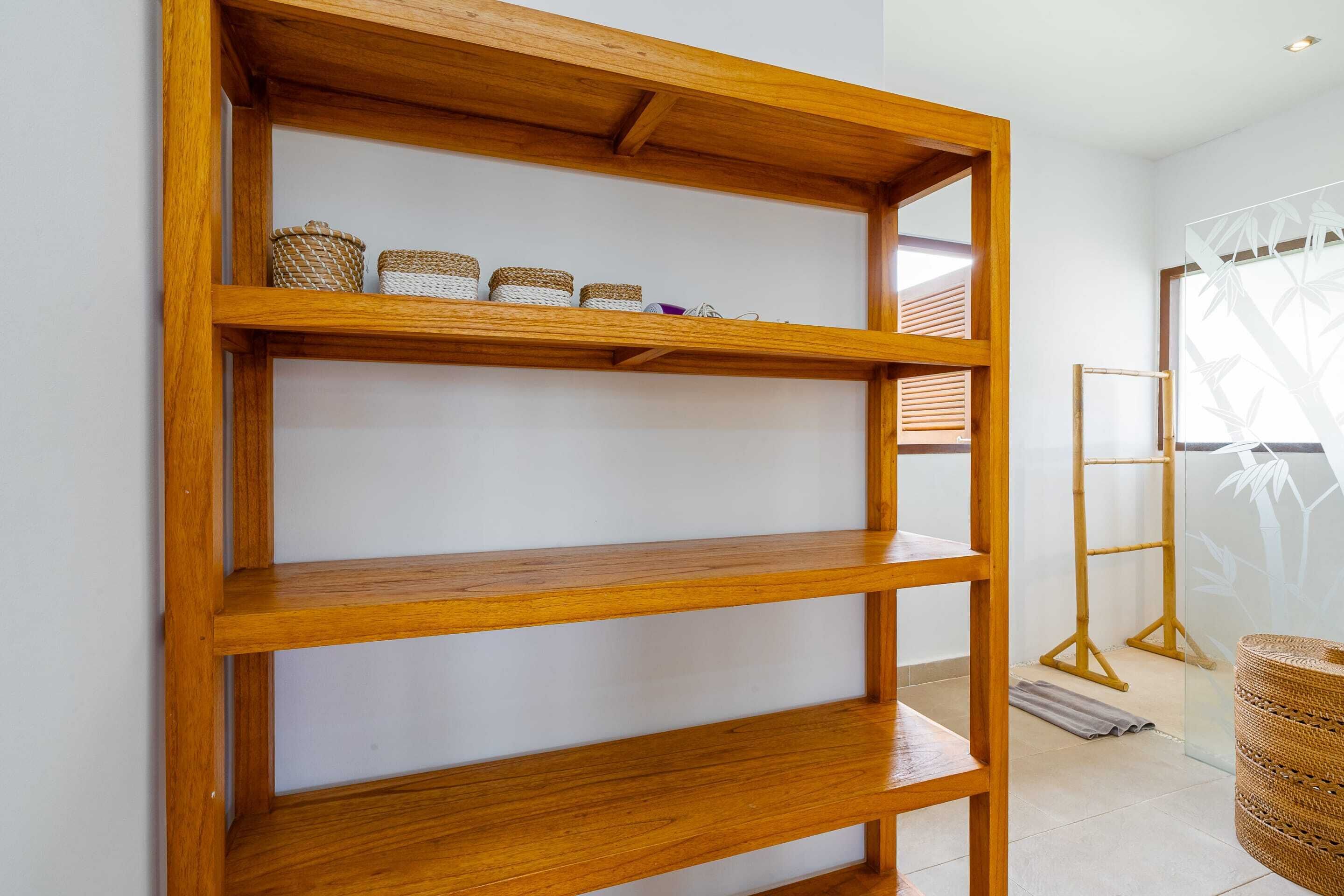A wooden shelf unit with baskets and a bamboo stand in a room with white walls and a window with a bamboo pattern.