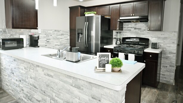 A modern kitchen with dark wooden cabinets, a stainless steel refrigerator, a built-in oven, and a granite countertop.