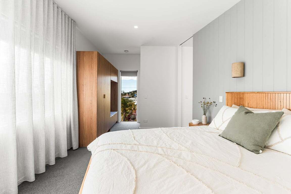 A modern bedroom with a large bed, a wooden headboard, and a view of the outdoors.