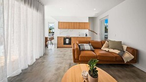Una sala moderna con un sofá de cuero marrón, una mesa de centro de madera con una planta y una cocina al fondo.