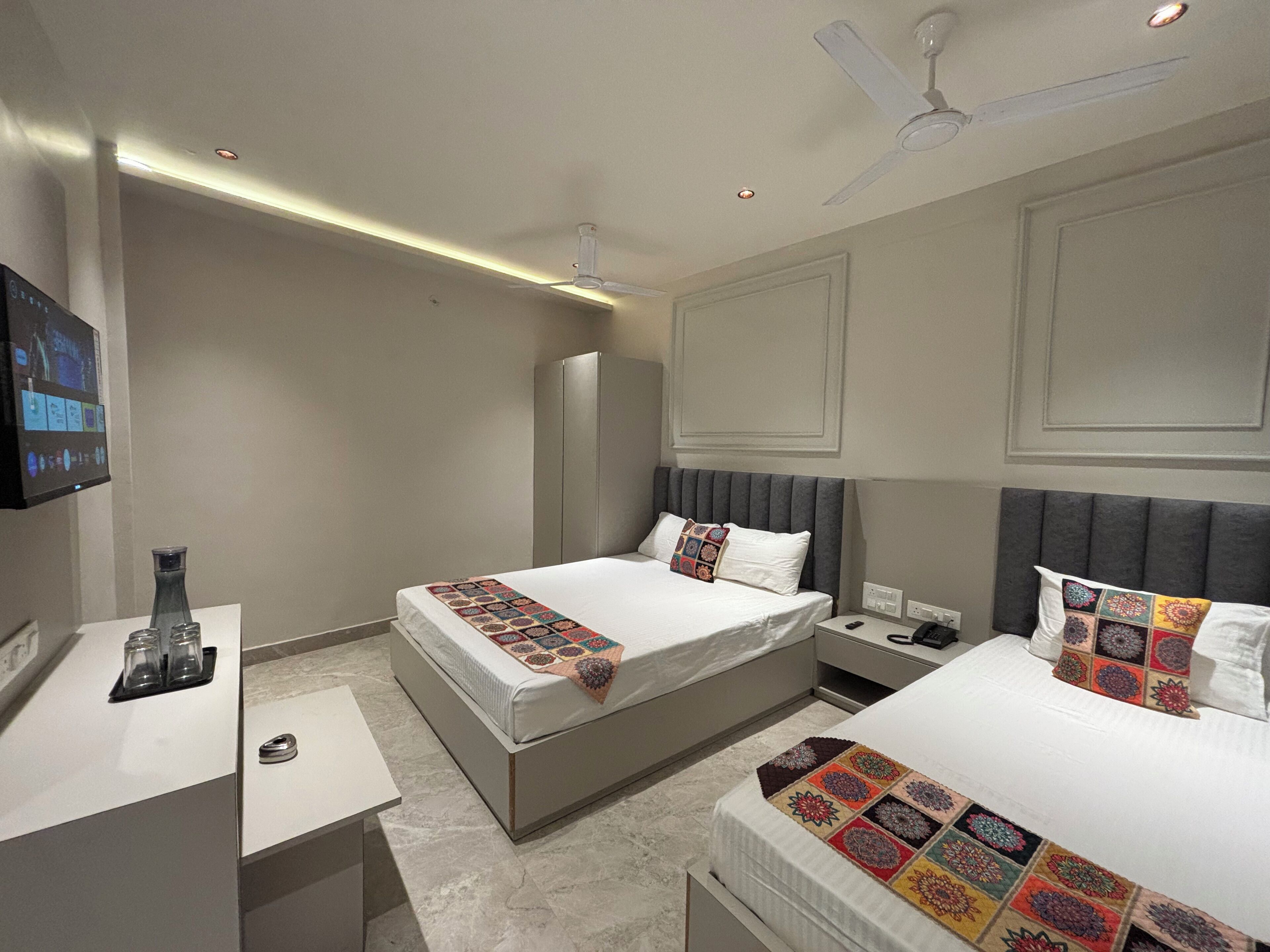 A hotel room with two beds, a TV, a desk, and a ceiling fan.