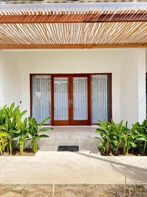 A modern house with a wooden pergola, a front door with glass panels, and potted plants on either side. - Turtle House 2 Lombok (Kuta)