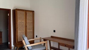 A minimalist room with a wooden chair, a wooden table, and a rattan wardrobe. - Turtle House 2 Lombok (Kuta)