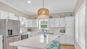 Een moderne keuken met witte kastjes, een groot eiland en een hanglamp.
