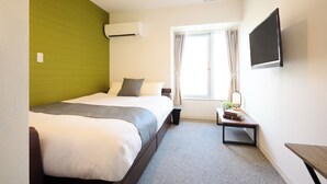 Een hotelkamer met een groot bed, een nachtkastje met een lamp, een aan de muur bevestigde televisie en een raam met gordijnen.