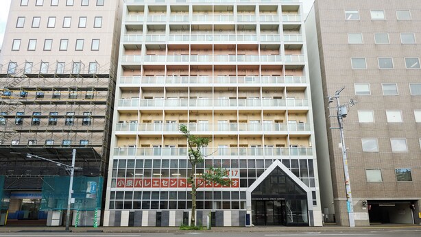 Een meerlaags hotel met een moderne gevel, met een opvallende ingang voorzien van een glazen luifel en een bord in een vreemde taal.