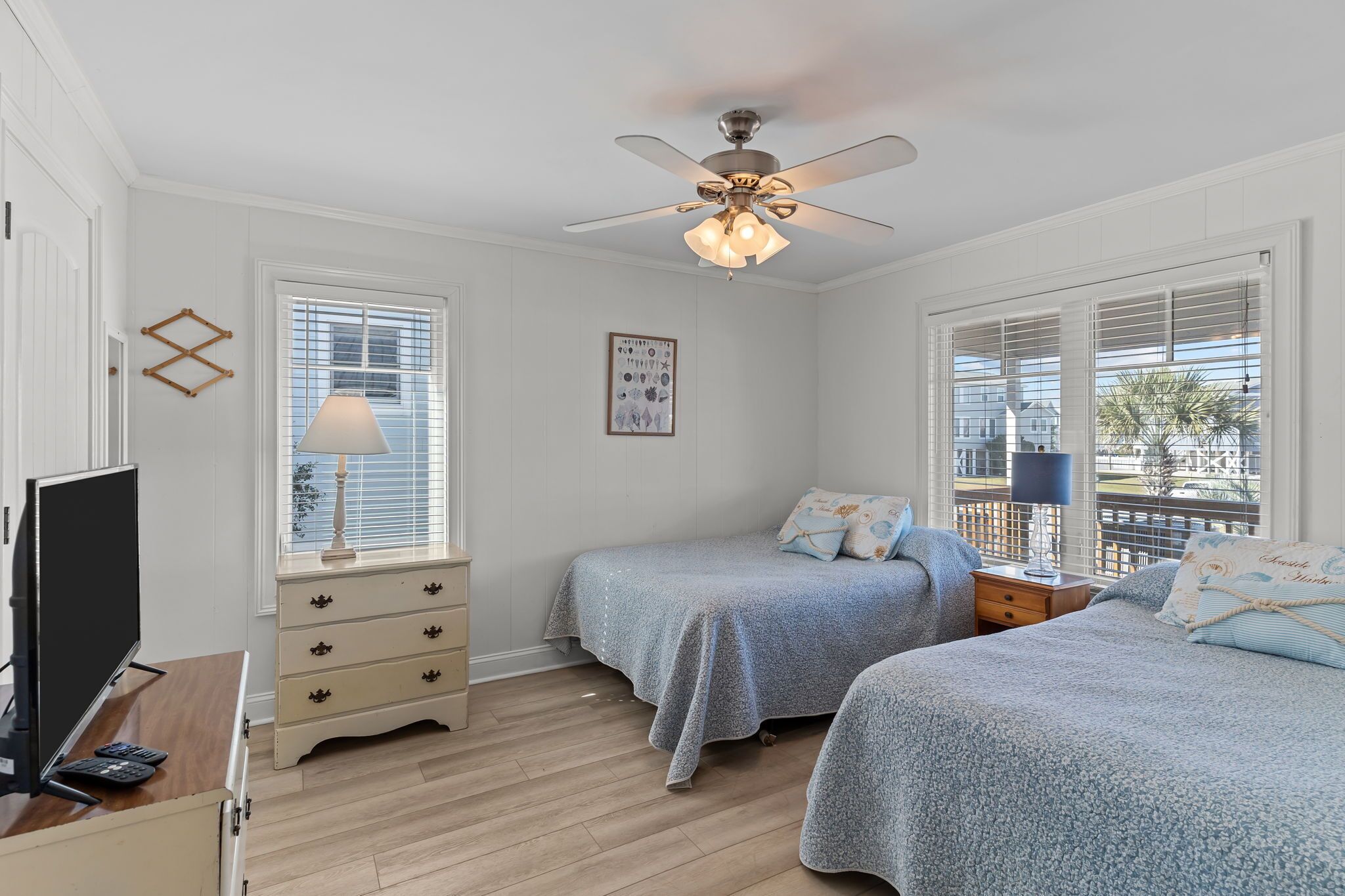 A bedroom with two beds, a ceiling fan, a TV, and a dresser.