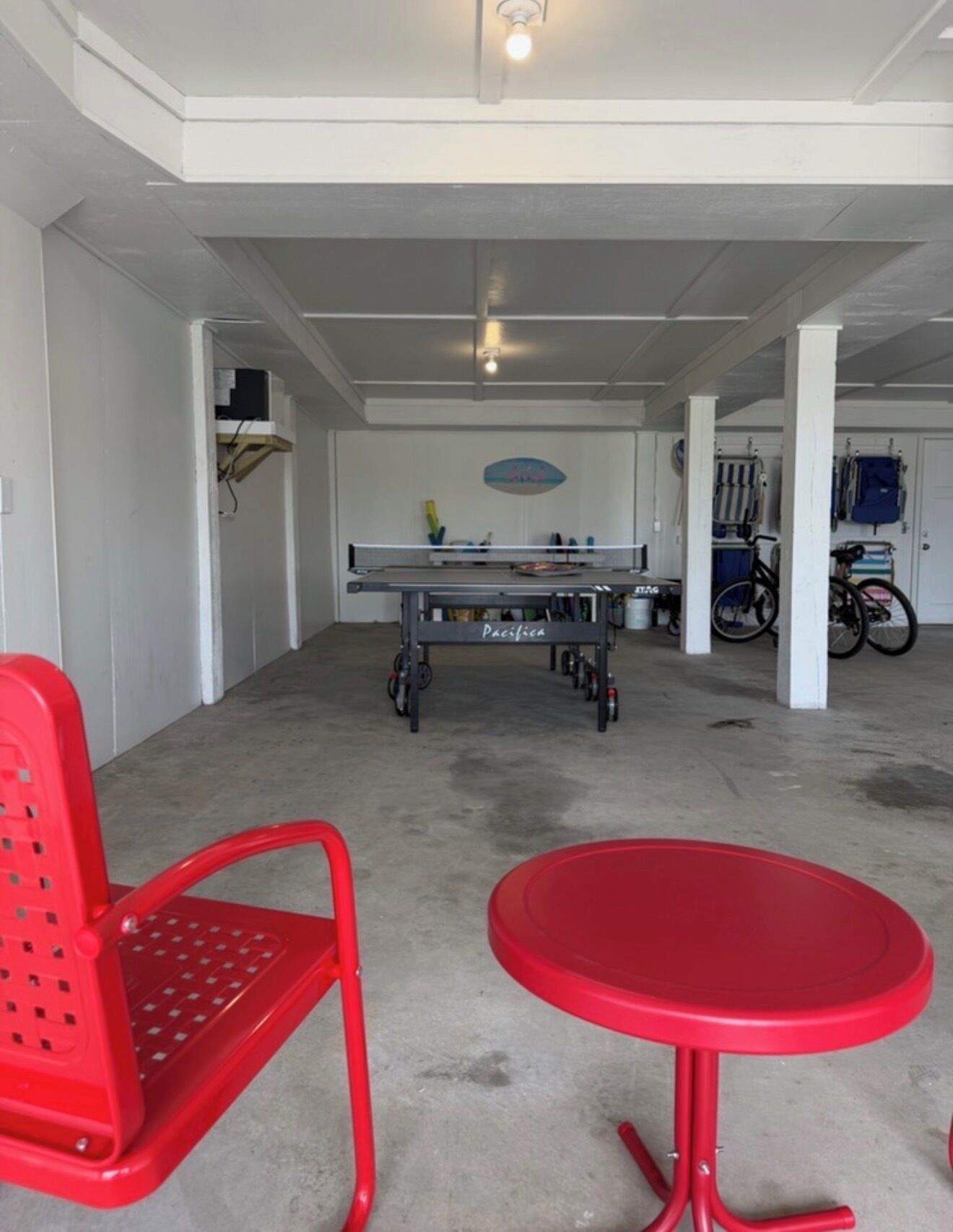 Habitació amb taula de ping-pong, cadires vermelles i bicicletes al fons.