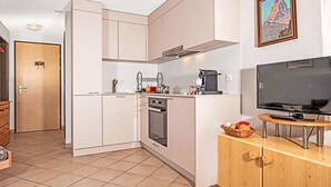 A compact kitchen with white cabinets, a stove, a coffee maker, and a TV on a wooden stand. - Apartment Laurin by Interhome (Zermatt)