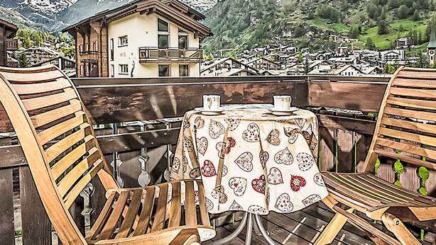 A wooden deck with a table and chairs, overlooking a mountain village with traditional buildings and a prominent peak in the background. - Apartment Laurin by Interhome (Zermatt)