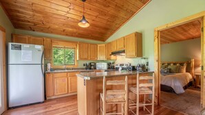 Une cabane en bois dotée d’une cuisine équipée d’un réfrigérateur, d’un four à micro-ondes et d’une cuisinière, ainsi que d’un petit coin bar avec des tabourets.